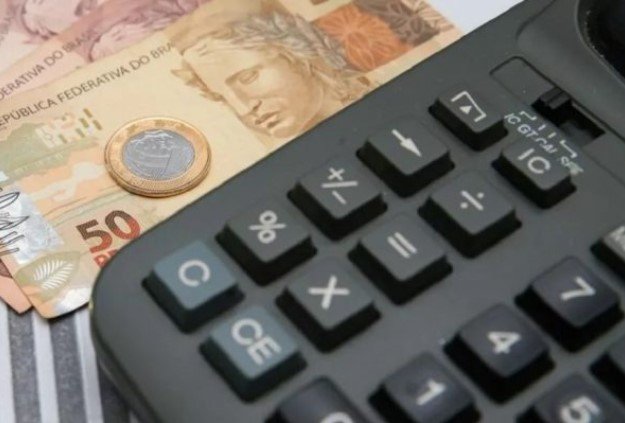 Cédulas e moedas ao lado de uma calculadora preta - Metrópoles