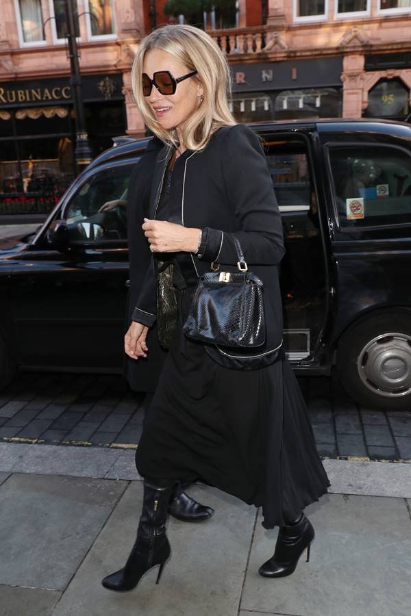 Mulher branca andando na rua com uma bolsa de couro preta