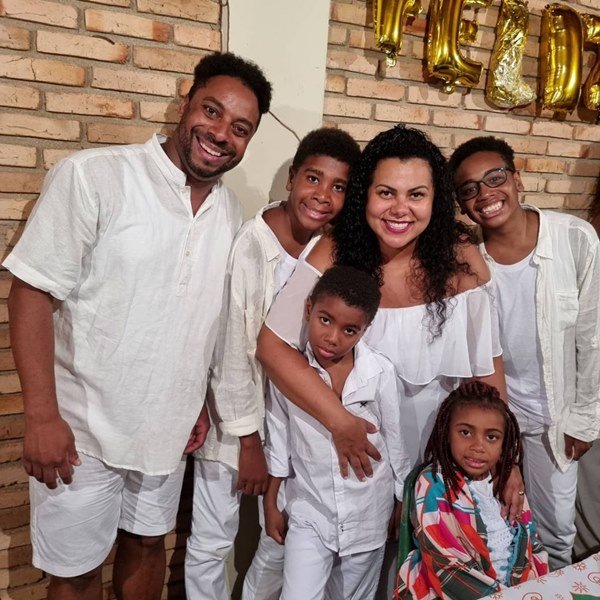 Mulher negra cercada dos quatro filhos e do marido. Todos usam branco