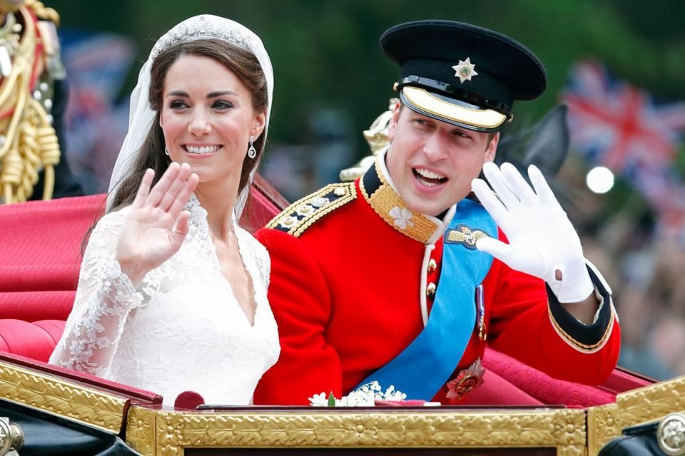 Foto colorida. Kate Middleton e príncipe William em uma carruagem