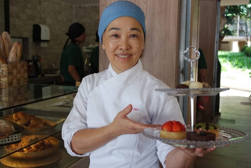 foto de chef com descendencia oriental que veste dolma branca e segura uma bandeja de doces