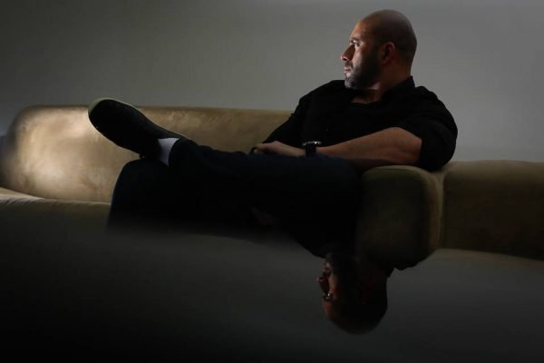 O deputado federal Daniel Silveira (PTB-RJ), sentado num sofá na penumbra, olha de perfil para frente - Metrópoles