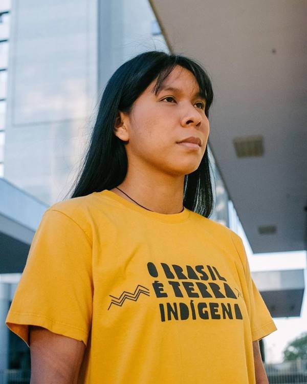 Mulher indígena posa usando camiseta com a frase "O Brasil é terra indigena" 