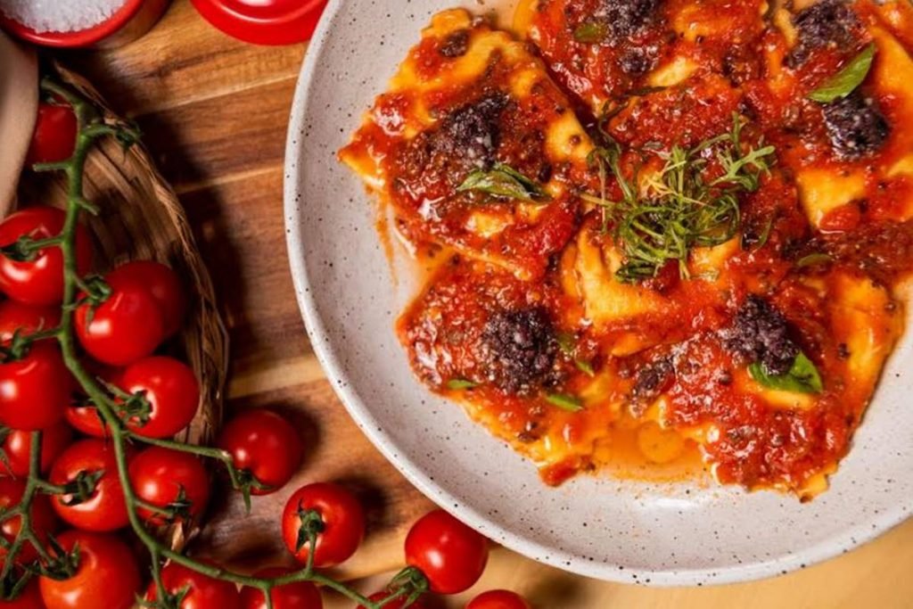 foto de prato com massa recheada e coberta de molho de tomate e tomatinhos ao lado