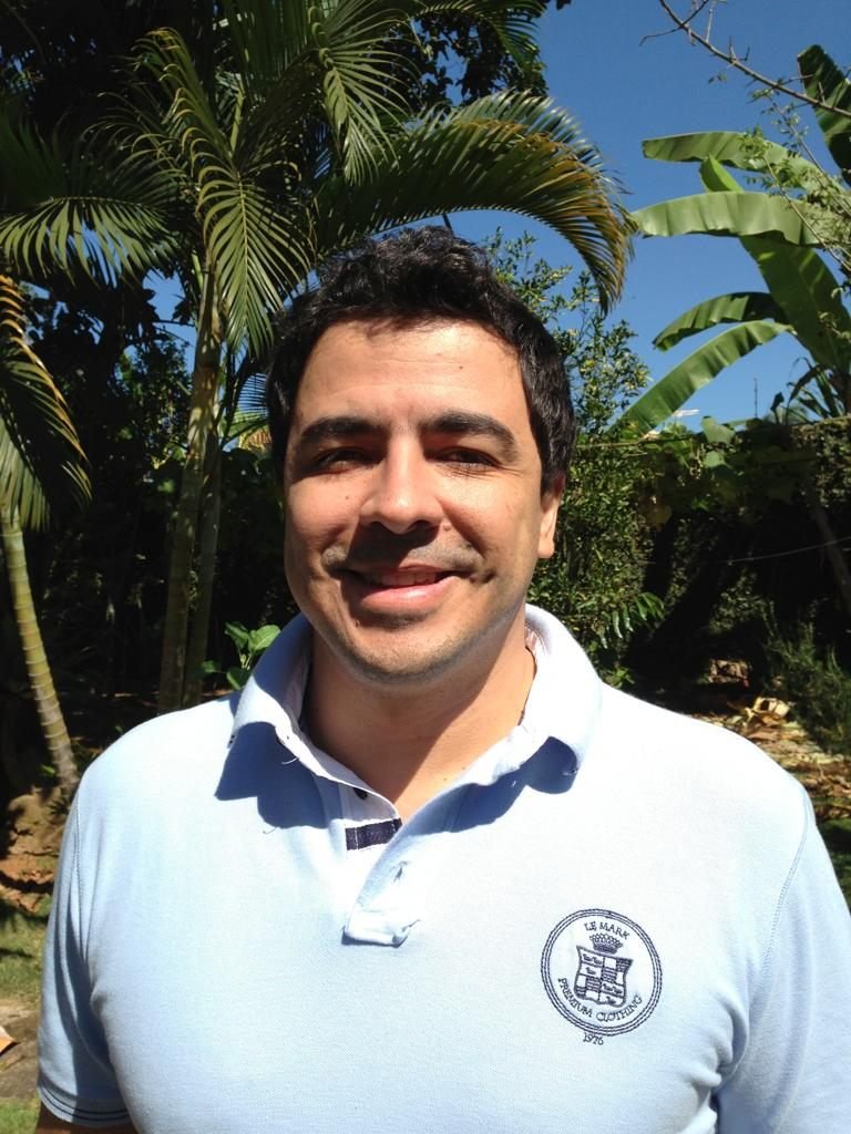 Homem vestindo blusa azul sorri para a foto. Alessandro Oliveira da Conceição