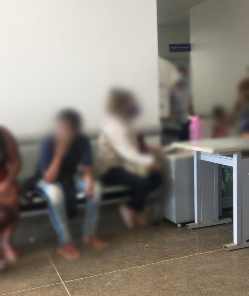 Pessoas com rosto borrado sentadas em cadeiras em frente a parede branca e ao lado de corredor