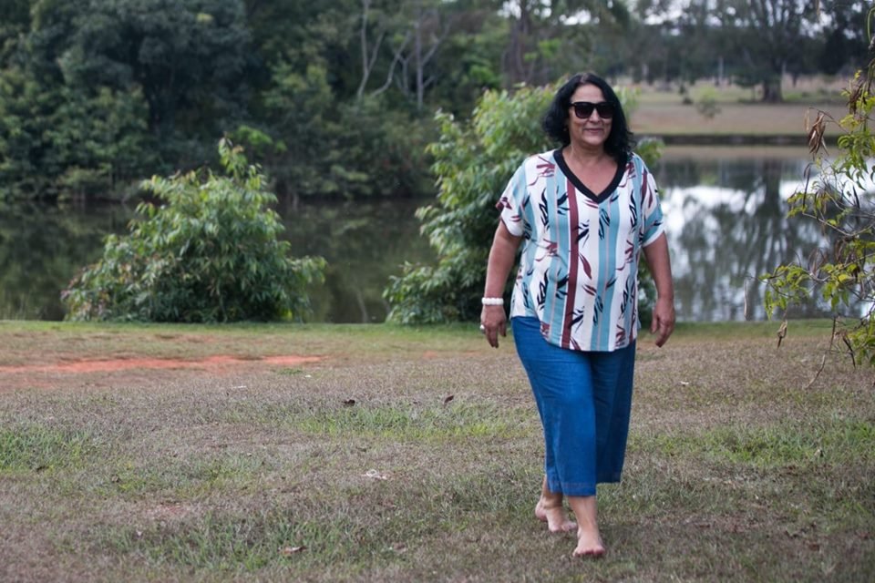 Mulher com blusa larga e calça azul usando óculos escuro e caminhando em parque