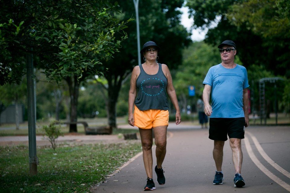 Homem e mulher ao lado um do outro, de boné e roupas de caminhada andando em pista no parque