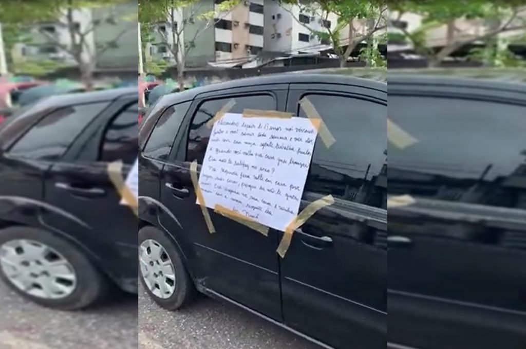 foto de uma cartolina pregada na lateral de um carro preto com fita adesiva