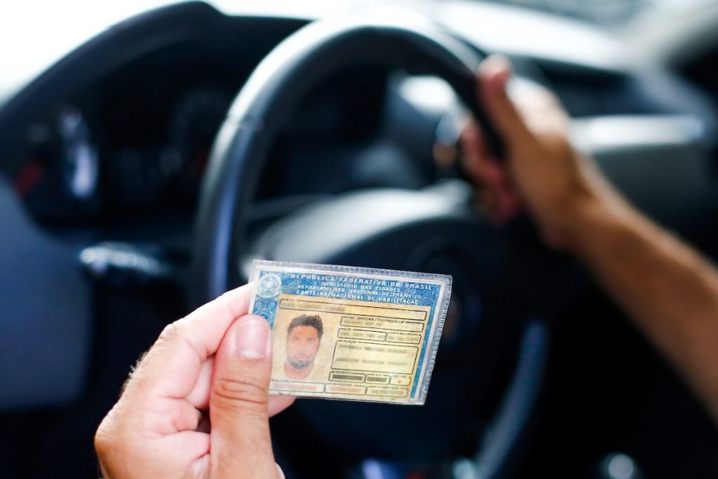 pessoa segura CNH enquanto está no carro com outra mão no volante