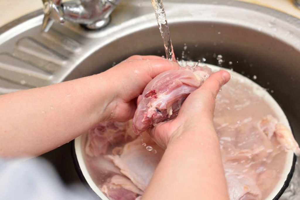 foto de bacia em pia e mao lavando pedaço de frango