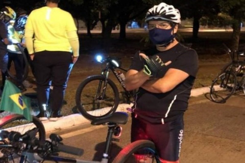 Homem de máscara e capacete próximo a bicicletas em rua à noite