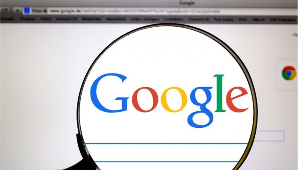 foto ilustrativa de uma pessoa usando uma lupa pare ver a logo do Google no computador