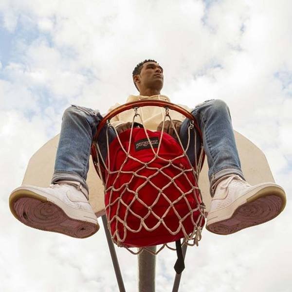 Homem jovem negro em cima de uma cesta de basquete com a mochila vermelha Jansport