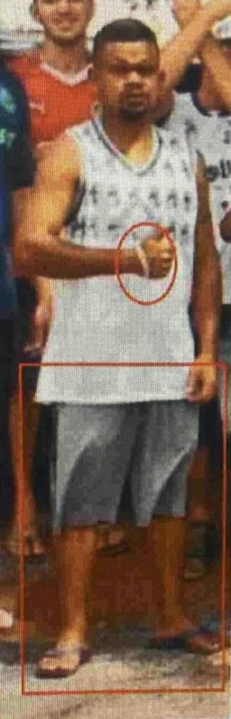 Homem negro, de regata branca faz sinal de joia para a câmera