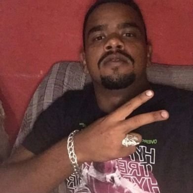 Homem negro com pulseira e anel de prata vestindo camisa preta em um fundo vermelho