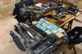 Conteúdo apreendido na casa do policial penal Alcimar Badaró Jacques, o Badá em operação do MPRJ. Sob mesas, vários maços de dinheiro, facões, facas, armas, coletes à prova de balas, projéteis e outros materiais - Metrópoles