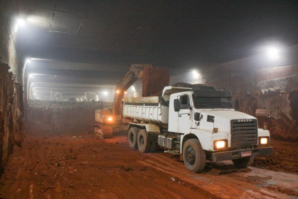 caminhão branco recebe terra de escavadeira em túnel
