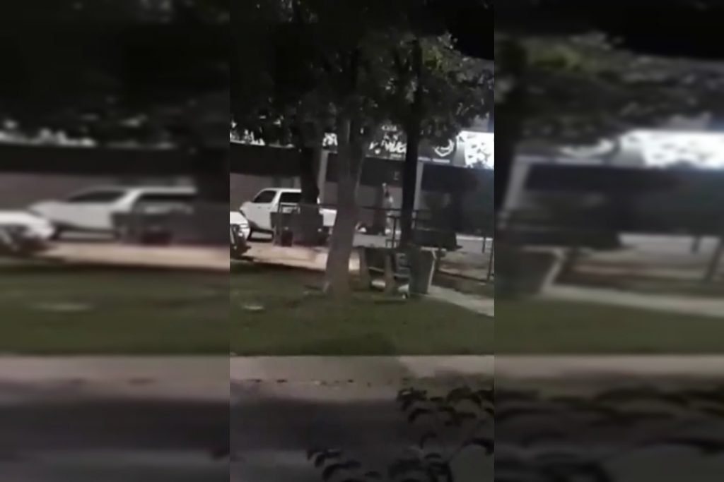 Homem camisa branca ataca outro homem, com fachada, em estacionamento de comércio