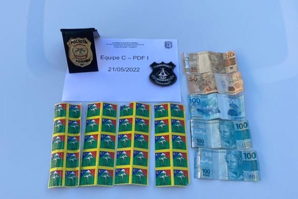 Selos de LSD, notas de 100 e 50 reais, folha de papel e distintivo da Polícia Penal do DF