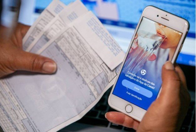 Pessoa segurando conta de água e celular - Metrópoles