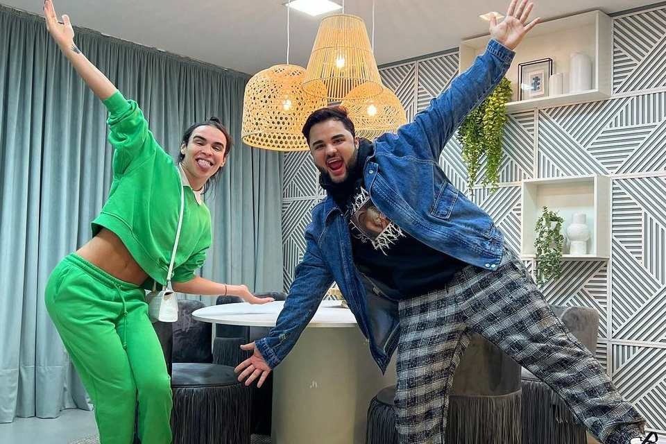 Lucas Guedez e Rafael Uccman em estúdio de seu novo programa, PocCast. O lugar é intimista, com cortina e paredes em tons claros, mesa redonda e cadeiras com franjas cinzas - Metrópoles
