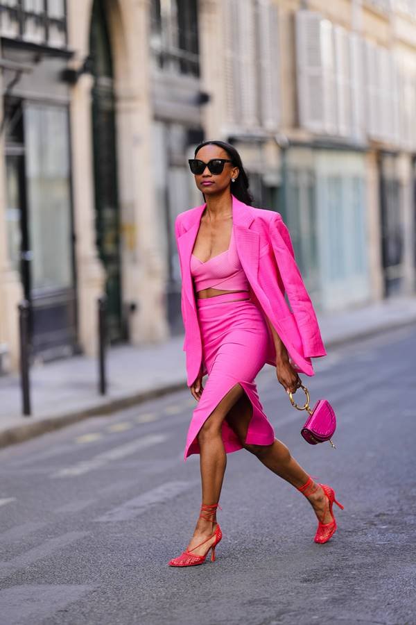 Look com saia, cropped, blazer, bolsa pequena e sandália de salto; tudo em rosa