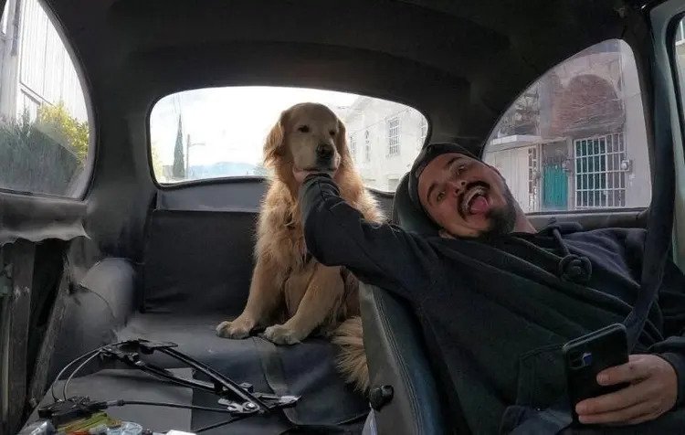 Foto colorida de um homem dentro de um carro com o cachorro