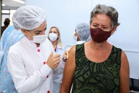 Mulher idosa sendo vacinada por profissional de saúde. Ambas usam máscara - Metrópoles