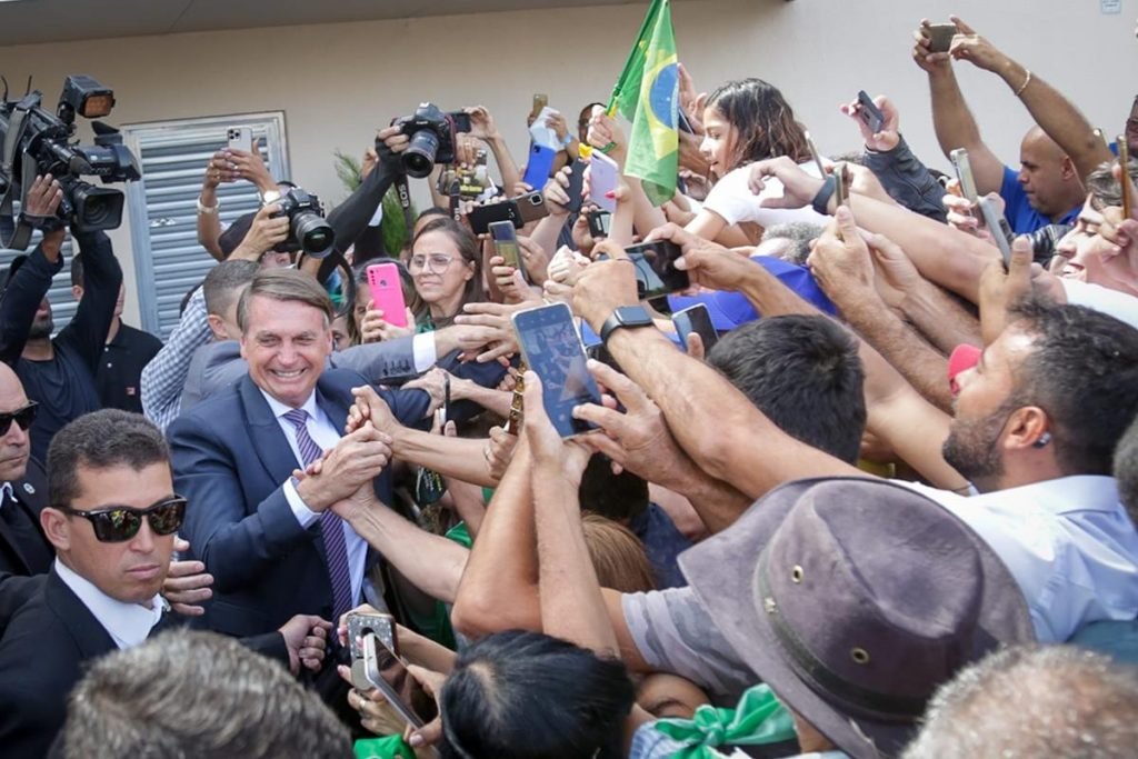 O presidente Bolsonaro durante motociata em Goiânia, onde também participou de evento evangélico. Ele cumprimenta apoiadores, cercado de multidão - Metrópoles