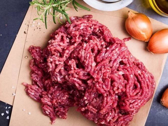 Carne moída sob tábua com sal grosso salpicado, cebolas e alecrim em volta - Metrópoles