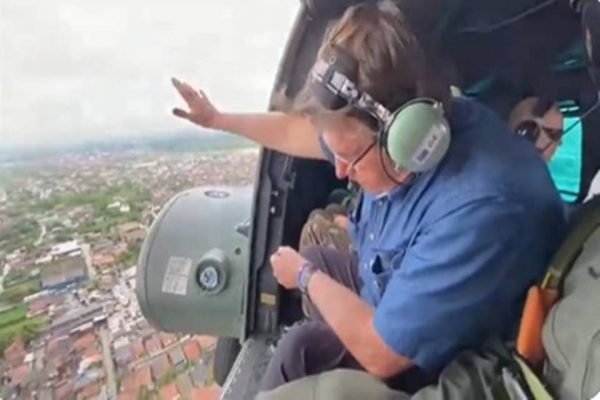 Bolsonaro sobrevoa Recife de helicóptero, acenando para as pessoas embaixo. É possível ver parte da cidade - Metrópoles