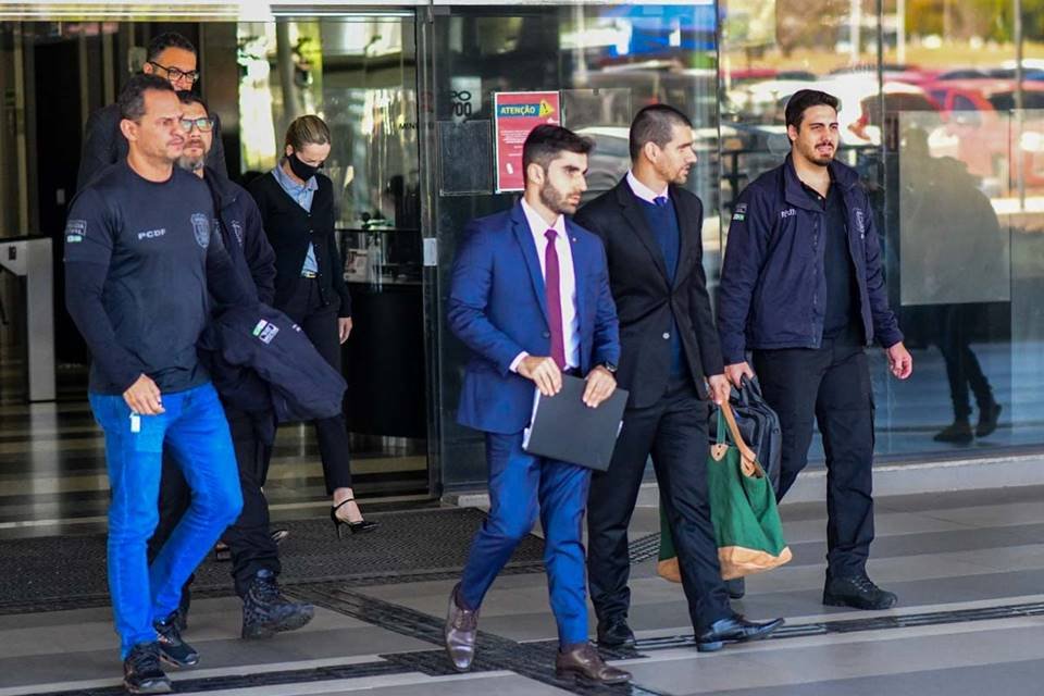 homens de terno e roupas variadas com pastas na mão saindo de um prédio