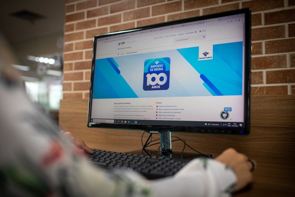 Pessoa fazendo a declaração de imposto de renda num computador vista de costas - Metrópoles