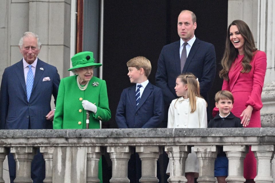 Foto colorida.  Rainha Elizabeth, príncipe Charles, príncipe William, príncipe George, princesa Charlotte, príncipe Louis e Kate Middleton