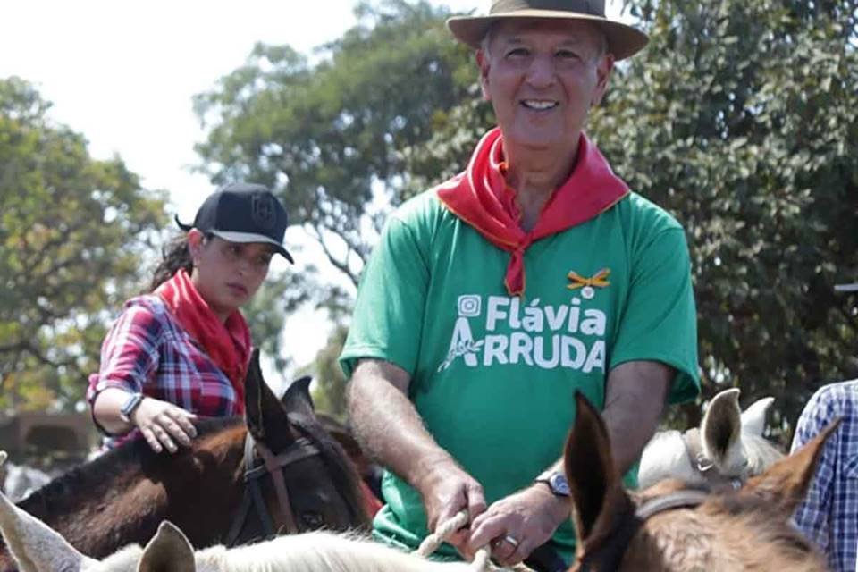homem de camiseta verde e lenço vermelho montado em cavalo com mulher ao fundo
