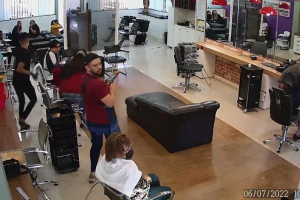 Homem de blusa vermelha reage a carro invadindo barbearia. Foto colorida