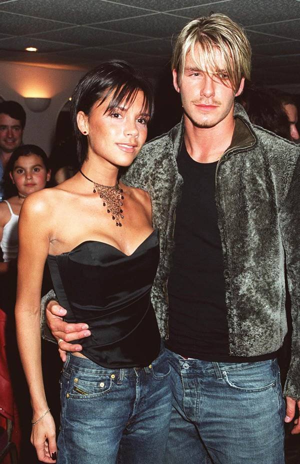 David e Victoria Beckham. Ela usa corset preto com colar longo e ele usa camiseta preta com casaco de veludo 