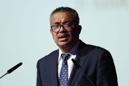 diretor-geral da OMS falando em microfone com fundo branco