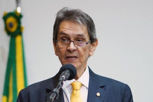O ex-presidente do PTB, Roberto Jefferson, fala num microfone com a bandeira do Brasil atrás - Metrópoles
