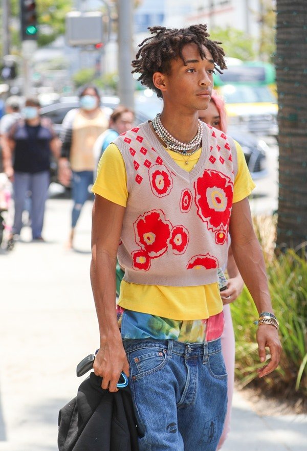 O ator e cantor Jaden Smith, um jovem rapaz negro com cabelos trançados, andando pelas ruas de Los Angeles. Ele veste uma camiseta amarela, com colete bege e vermelho, e calça jeans folgada.