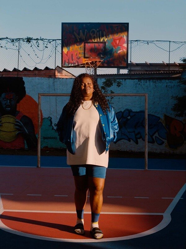 Na imagem com cor, mulher negra posa em quadra de basquete para videoclipe da Rider