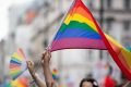Pessoas levantando bandeiras e objetos com cores arco-íris, símbolo LGBTQ+, em manifestação de rua - Metrópoles