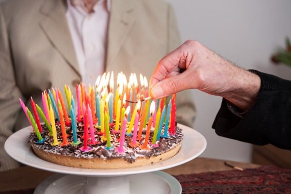 idoso acendendo velas de aniversário coloridas em um bolo