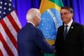 O presidente Bolsonaro cumprimenta o presidente americano Joe Biden na Cúpula das Américas, apertando as mãos. Ao fundo, as bandeiras dos Estados Unidos e Brasil - Metrópoles