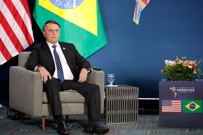 O presidente Bolsonaro sentado em uma poltrona durante uma reunião bilateral com o presidente americano Joe Biden na Cúpula das Américas Ao fundo, as bandeiras dos Estados Unidos e Brasil - Metrópoles
