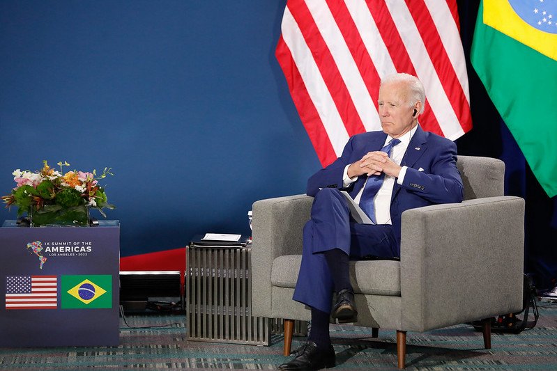 O presidente Joe Biden sentado na poltrona durante reunião bilateral com Bolsonaro na Cúpula das Fundos Ao América, as bandeiras dos Estados Unidos Brasil - Merópoles