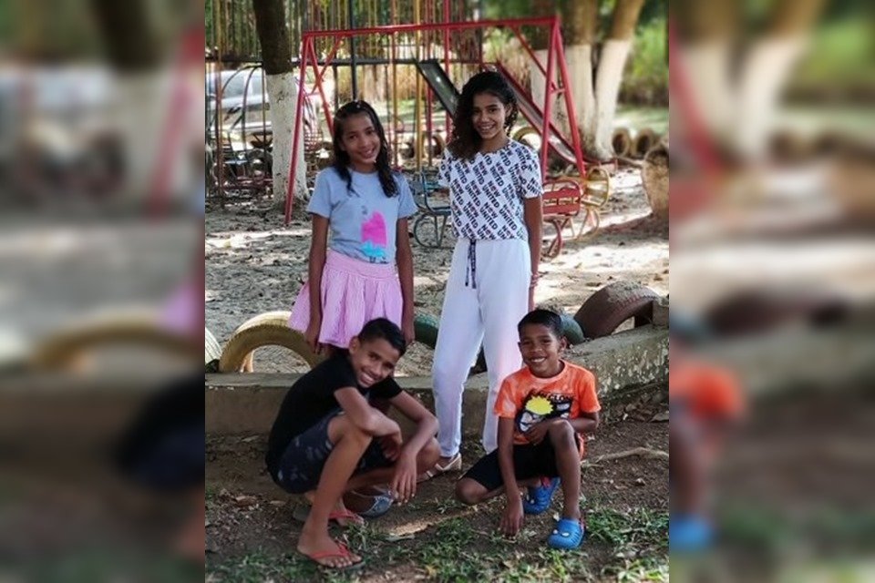 Duas meninas em pé e dois meninos abaixados em parquinho