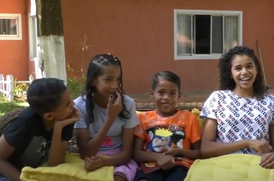 Dois meninos e duas meninas sentados em sofá em frente de casa laranja