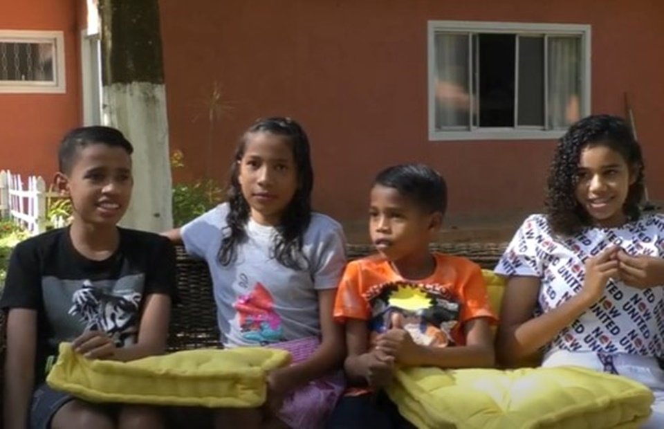 Dois meninos e duas meninas sentados em sofá em frente de casa laranja